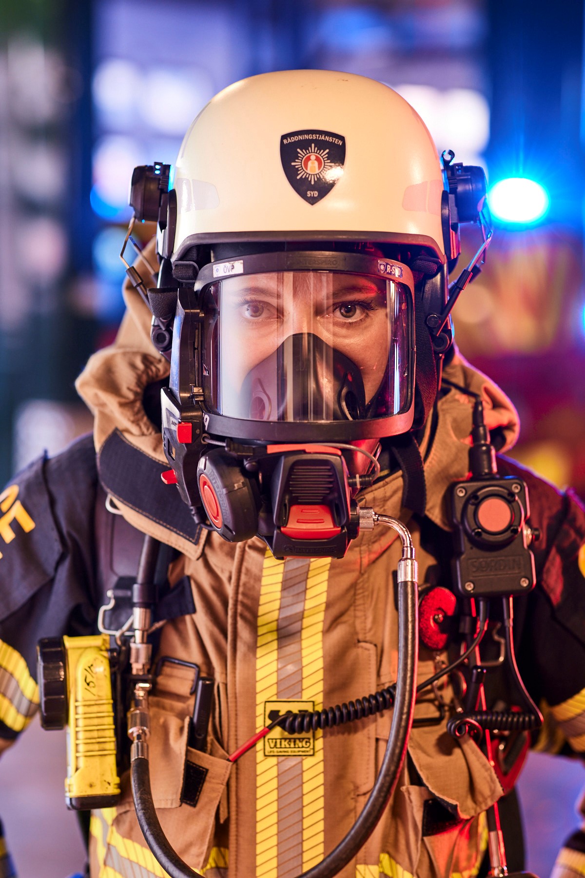 Brandman i larmställ och andningsskydd med blåljus i bakgrunden